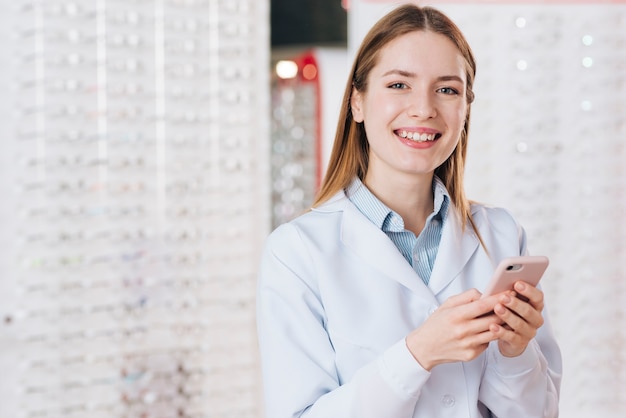 Ritratto dell&#39;optometrista femminile amichevole che per mezzo dello smartphone