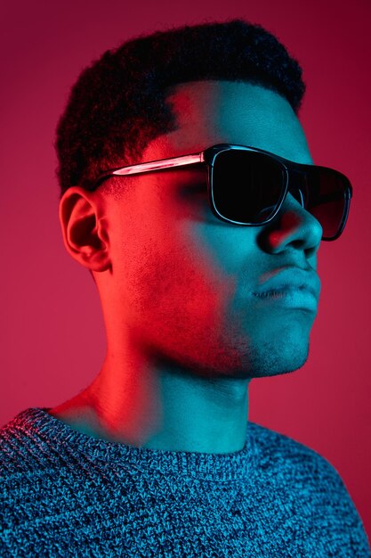 Ritratto dell'uomo afroamericano isolato su sfondo rosso per studio in luce al neon multicolore