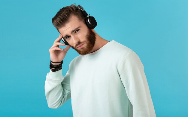 Ritratto dell'uomo barbuto che ascolta la musica sulle cuffie senza fili sull'azzurro