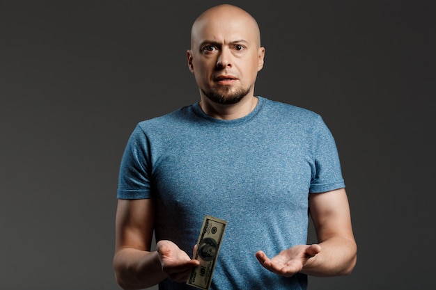 Ritratto dell'uomo bello in camicia grigia che tiene soldi sopra la parete scura