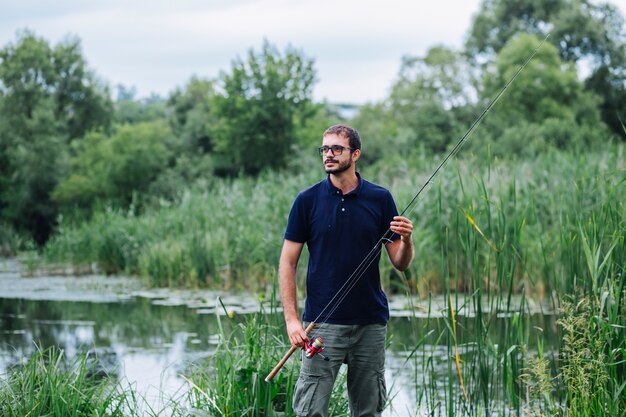 Ritratto dell&#39;uomo che sta vicino alla canna da pesca della tenuta del lago