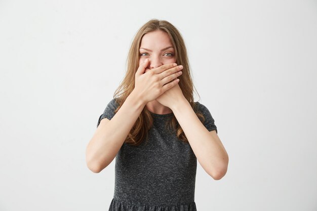 Ritratto della bocca di chiusura della giovane bella ragazza positiva dietro la mano.