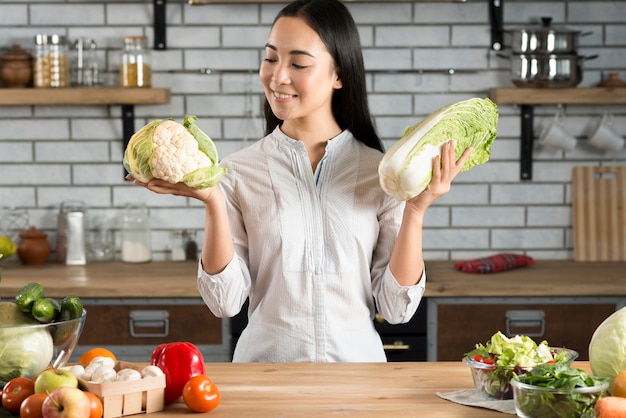 Ritratto della donna asiatica che tiene cavolfiore e lattuga verdi in cucina