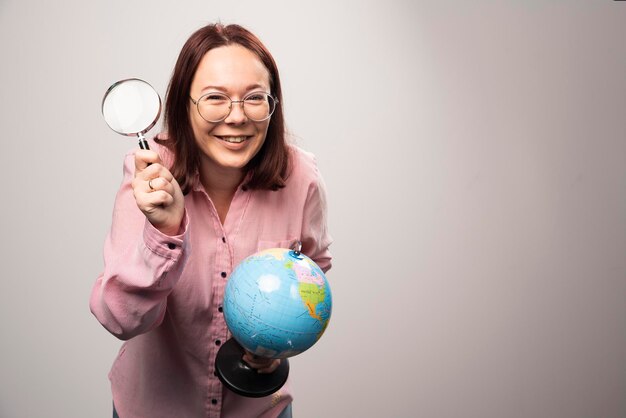 Ritratto della donna che tiene una lente d'ingrandimento e un globo terrestre. Foto di alta qualità