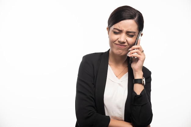 Ritratto della donna di affari che parla sul telefono sulla parete bianca.