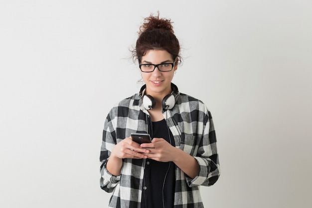 Ritratto della donna graziosa sorridente dei giovani pantaloni a vita bassa nella posa d'uso di vetro della camicia a quadretti isolata, tenente Smart Phone