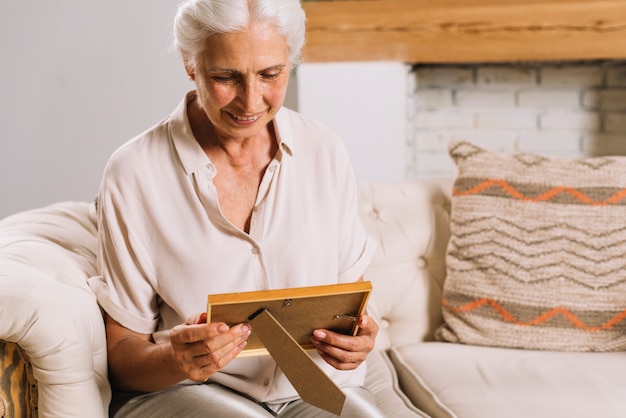 Ritratto della donna senior sorridente che si siede sul sofà che esamina la struttura della foto