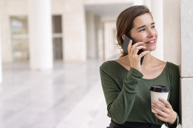 Ritratto della donna sorridente che parla sul telefono cellulare in corridoio