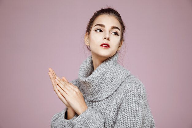 Ritratto della donna tenera in maglione grigio che scalda le mani sullo spazio rosa della copia