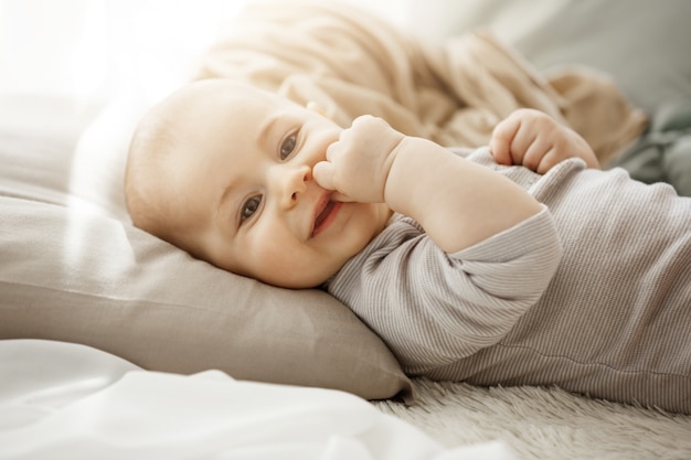 Ritratto della figlia neonata sorridente dolce che si trova sul letto accogliente. Il bambino guarda la telecamera e toccando il viso con le sue piccole mani. Momenti dell'infanzia.