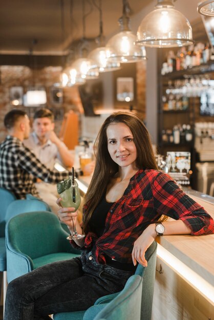 Ritratto della giovane donna attraente che si siede vicino al contro cocktail della tenuta del contatore