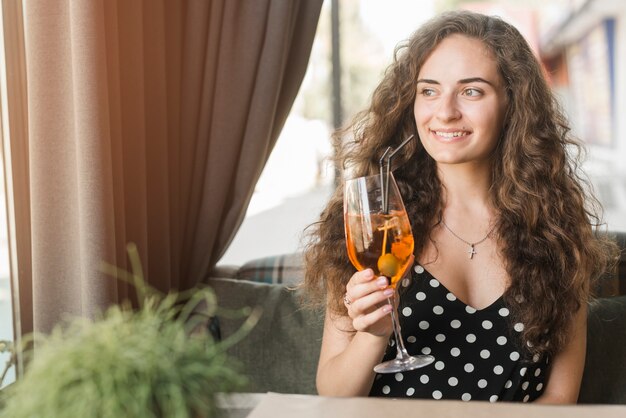 Ritratto della giovane donna attraente sorridente che tiene vetro del cocktail con oliva