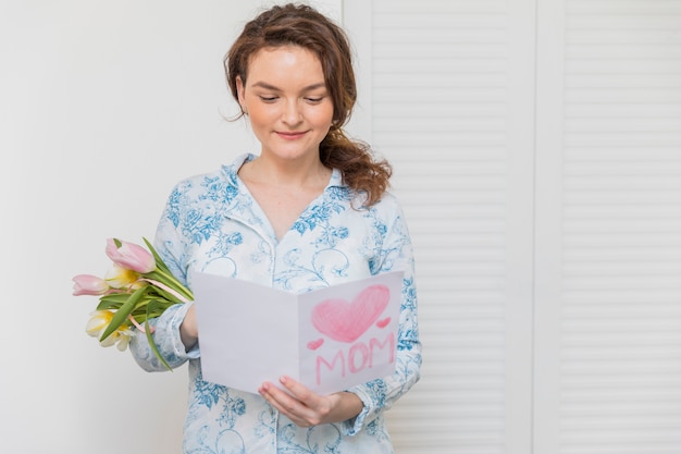 Ritratto della giovane donna felice che legge la cartolina d&#39;auguri con il mazzo del fiore del tulipano della tenuta