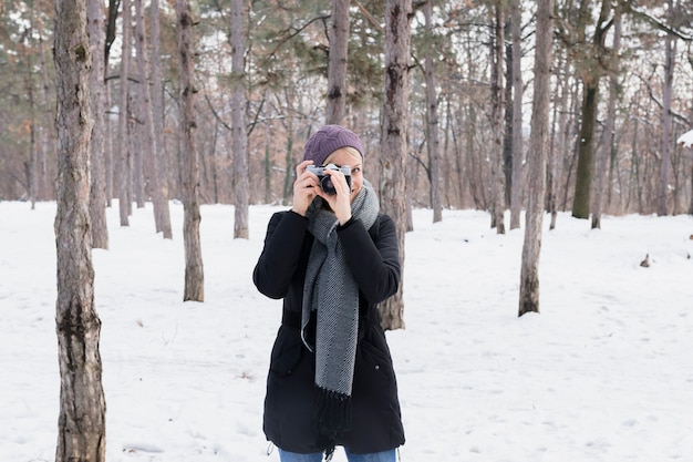 Ritratto della macchina fotografica della tenuta della giovane donna nel paesaggio nevoso