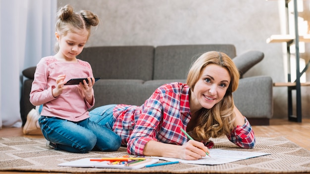 Ritratto della madre che attinge libro mentre figlia che per mezzo del cellulare