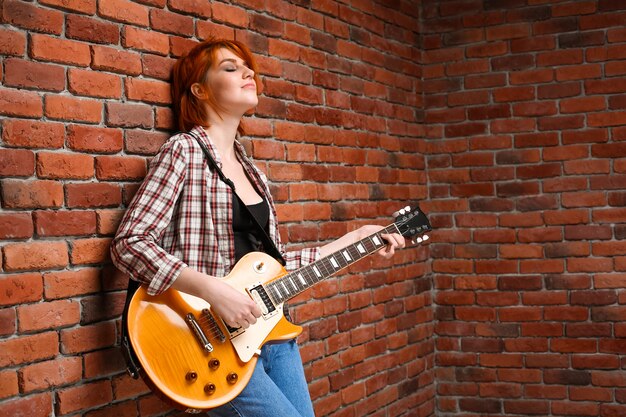 Ritratto della ragazza con la chitarra sopra il fondo del mattone.