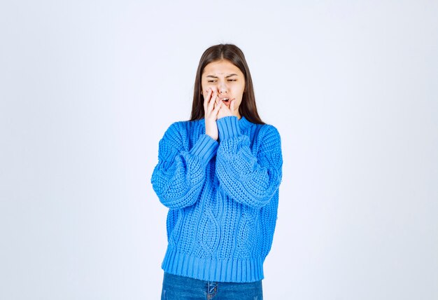 Ritratto della ragazza dell'adolescente in maglione blu che ha mal di denti su bianco.