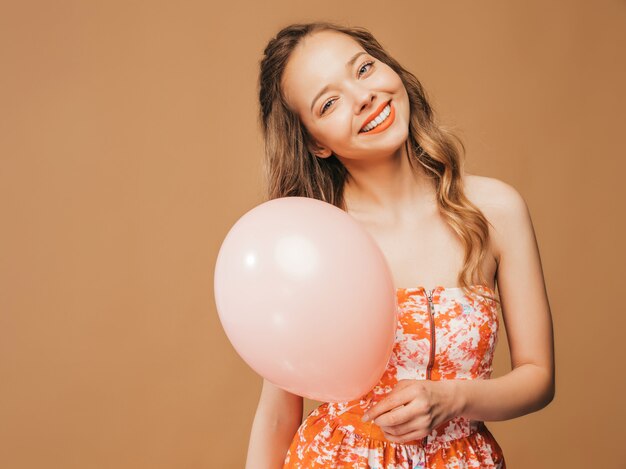 Ritratto della ragazza emozionante che posa in vestito variopinto da estate d'avanguardia. Donna sorridente con la posa rosa del pallone. Modello pronto per la festa