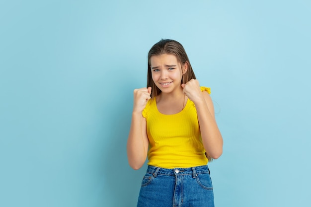 Ritratto della ragazza teenager caucasica isolato su priorità bassa blu. Bellissimo modello di capelli lunghi in abbigliamento casual.