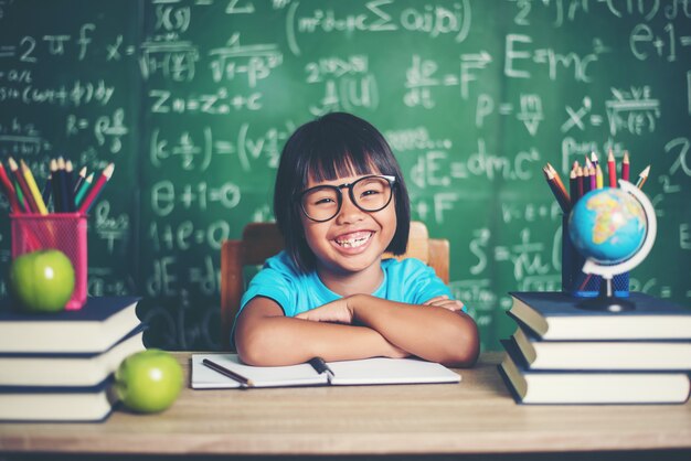 Ritratto della scolara sorridente che si siede al tavolo con i libri