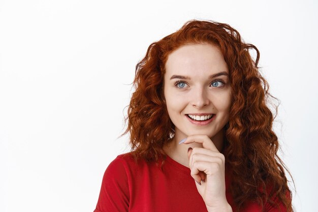 Ritratto della testa di una ragazza adolescente dai capelli rossi che guarda da parte premuroso avendo un'idea interessante vedere qualcosa di intrigante sullo sfondo bianco
