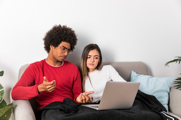 Ritratto delle coppie interrazziali facendo uso del computer portatile insieme