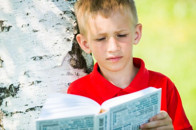Ritratto dello scolaro che legge il libro in natura