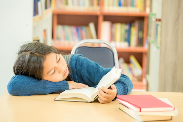 Ritratto dello studente abile con il libro aperto che lo legge nella biblioteca di istituto universitario