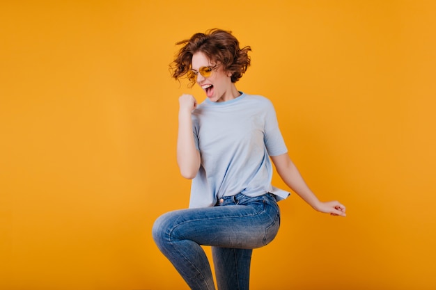 Ritratto dello studio di giovane donna graziosa in blue jeans che salta sullo spazio luminoso