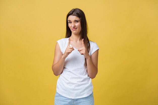 Ritratto deluso goffa donna attraente in camicia bianca alzando la mano e modellando un piccolo oggetto guardando le dita e accigliata per l'antipatia e il rimpianto in piedi su sfondo giallo