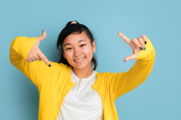 Ritratto di adolescente asiatico isolato su sfondo blu studio. Bellissima modella bruna femminile con i capelli lunghi in stile casual. Concetto di emozioni umane, espressione facciale, vendite, annuncio. Fa selfie.