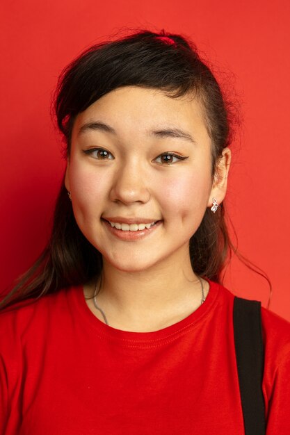 Ritratto di adolescente asiatico isolato su sfondo rosso studio. Bellissima modella bruna femminile con i capelli lunghi in stile casual. Concetto di emozioni umane, espressione facciale, vendite, annuncio. Sorridente carino.