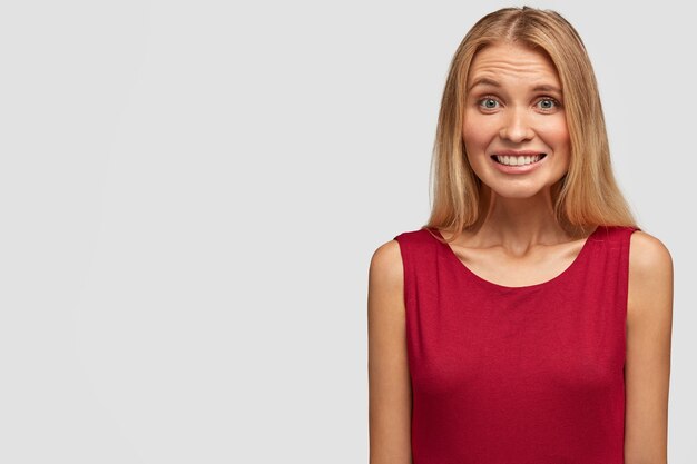 Ritratto di adorabile giovane donna in maglietta rossa, ridacchia, ha un sorriso a trentadue denti, mostra i denti bianchi perfetti