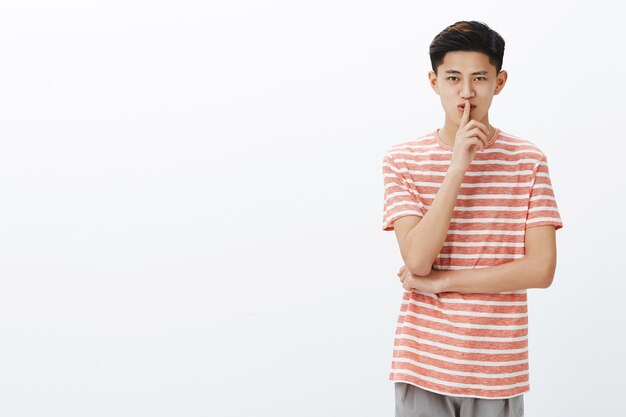 Ritratto di affascinante misterioso giovane adolescente asiatico con acconciatura corta che mostra gesto di silenzio e sorridente con sorpresa o condivisione segreto