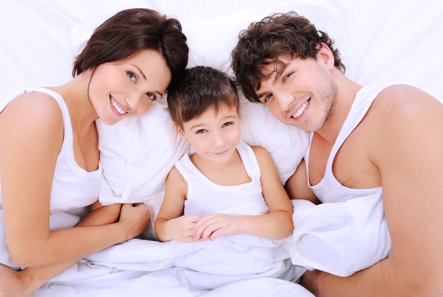 Ritratto di alto angolo dei genitori sorridenti felici con il ragazzino sdraiato su un letto