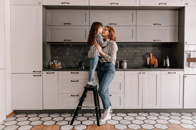 Ritratto di bambina sta sulle scale e abbraccia la madre in cucina.