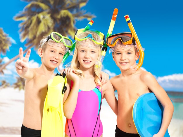 Ritratto di bambini felici che godono in spiaggia. Scolari bambini in piedi insieme in costume da bagno di colore brillante con maschera da nuoto sulla testa.