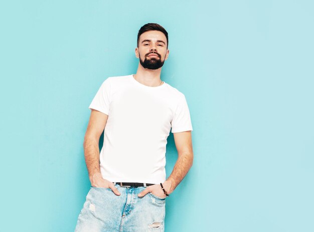 Ritratto di bel modello lambersexual hipster elegante e sicuro di sé vestito di maglietta bianca e jeans Moda maschile isolato su parete blu in studio