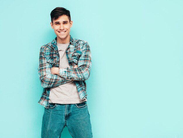 Ritratto di bel modello sorridente Uomo alla moda sexy vestito con jeans e camicia a scacchi Moda maschio hipster in posa vicino al blu in studio isolato