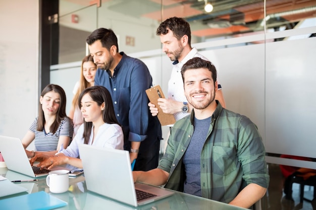 Ritratto di bell'uomo latino in casual seduto con i colleghi che lavorano sul retro