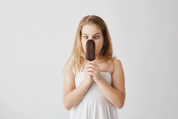 Ritratto di bella bambina bionda con gli occhi azzurri affascinanti che posa sciocca con il gelato in sue mani mentre papà che prende le immagini per l'album di foto della famiglia.