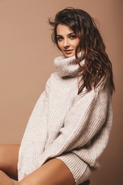 Ritratto di bella dolce carina donna bruna sorridente. Ragazza in maglione casual grigio. Modello in posa in studio. Seduto sulla sedia