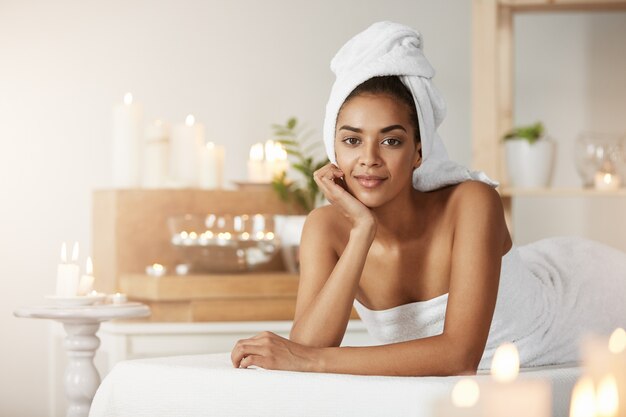 Ritratto di bella donna africana con asciugamano sulla testa di riposo sorridente nel salone spa.