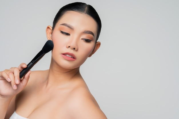 Ritratto di bella donna asiatica che tiene il pennello per fard per il trucco