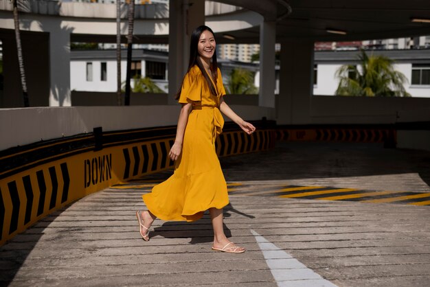 Ritratto di bella donna asiatica in vestito giallo che posa all'aperto nella città