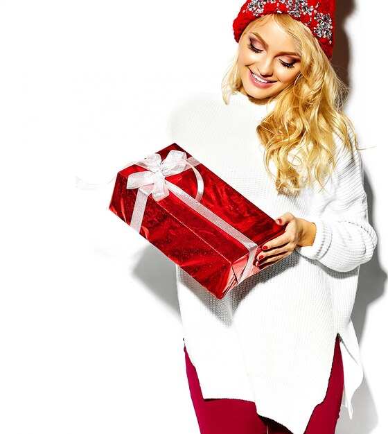 Ritratto di bella donna bionda sorridente dolce felice che tiene in mano grande confezione regalo di Natale in abiti invernali casual rosso hipster, in maglione bianco caldo