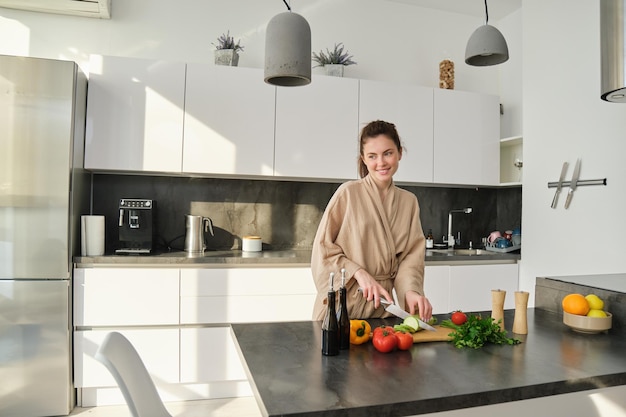 Ritratto di bella donna che cucina insalata in cucina tagliando le verdure e sorridendo nella preparazione