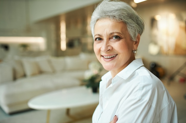 Ritratto di bella donna di affari matura dai capelli grigi in camicia bianca che si siede all'ingresso dell'hotel