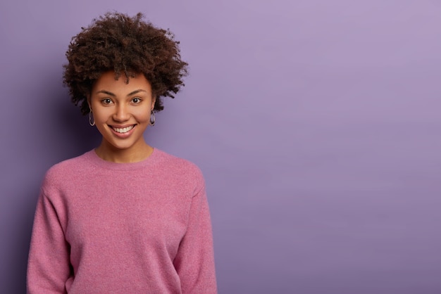 Ritratto di bella donna felice ha i capelli afro, sorride con gioia, riceve piacevoli notizie