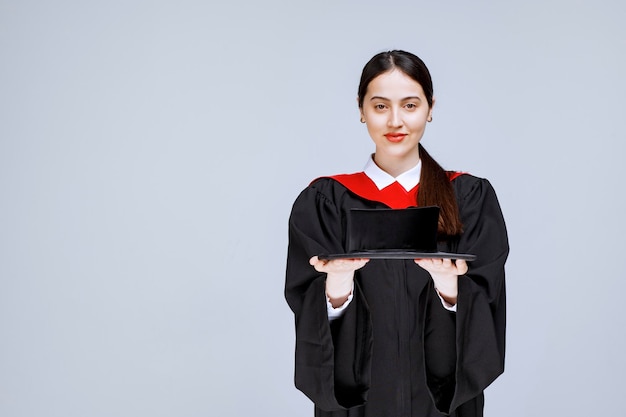 Ritratto di bella donna in abito di laurea in piedi sopra il muro. Foto di alta qualità